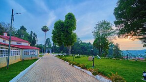 A paved pathway leading to a building with a red roof, surrounded by greenery and trees. - Mowbray House Resort Ooty by VOYE HOMES (Ooty)