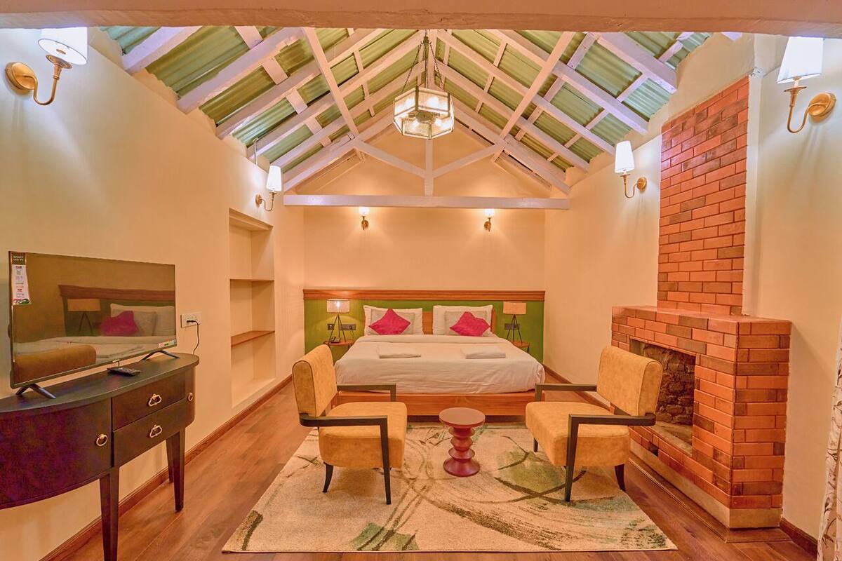 Quarto com uma cama grande, duas cadeiras, uma mesa pequena, TV sobre um aparador e lareira de tijolos.