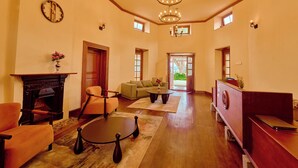 A spacious living room with a fireplace, sofas, a coffee table, and a desk. - Mowbray House Resort Ooty by VOYE HOMES (Ooty)