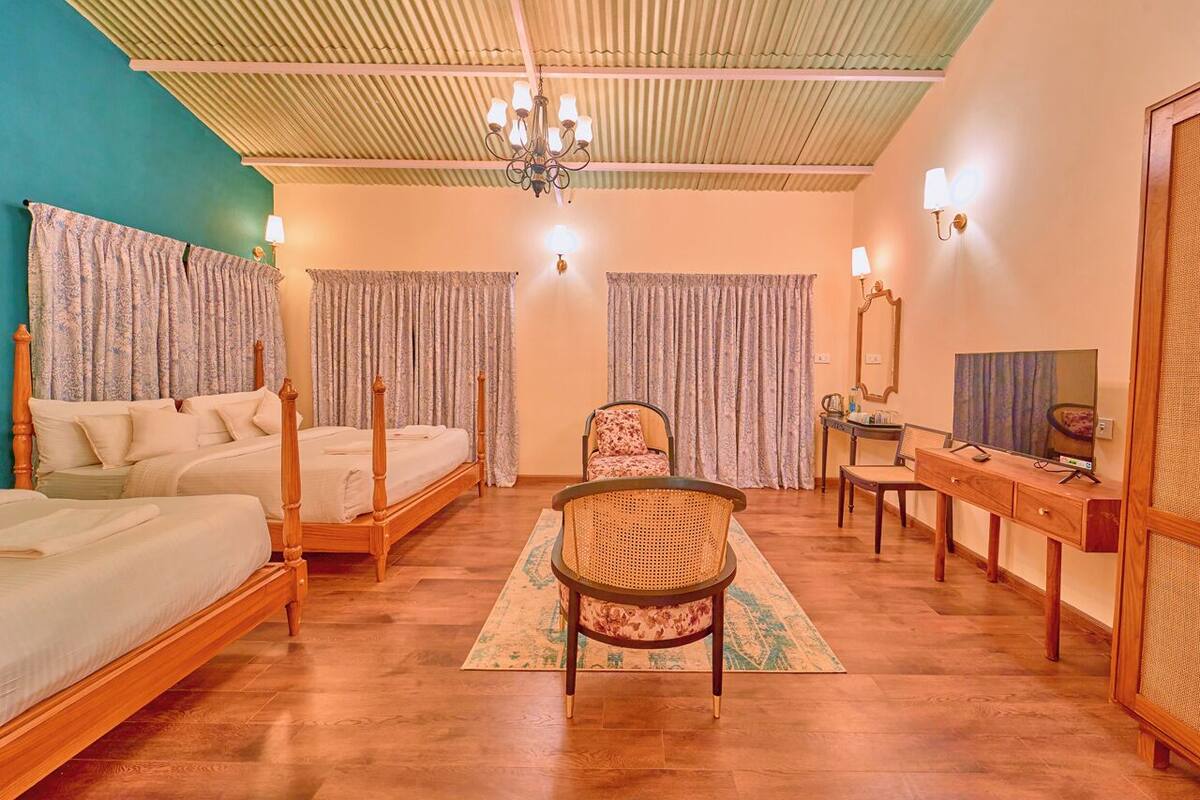 Quarto de hotel com duas camas de madeira, uma cadeira de vime, uma escrivaninha com espelho e uma televisão.