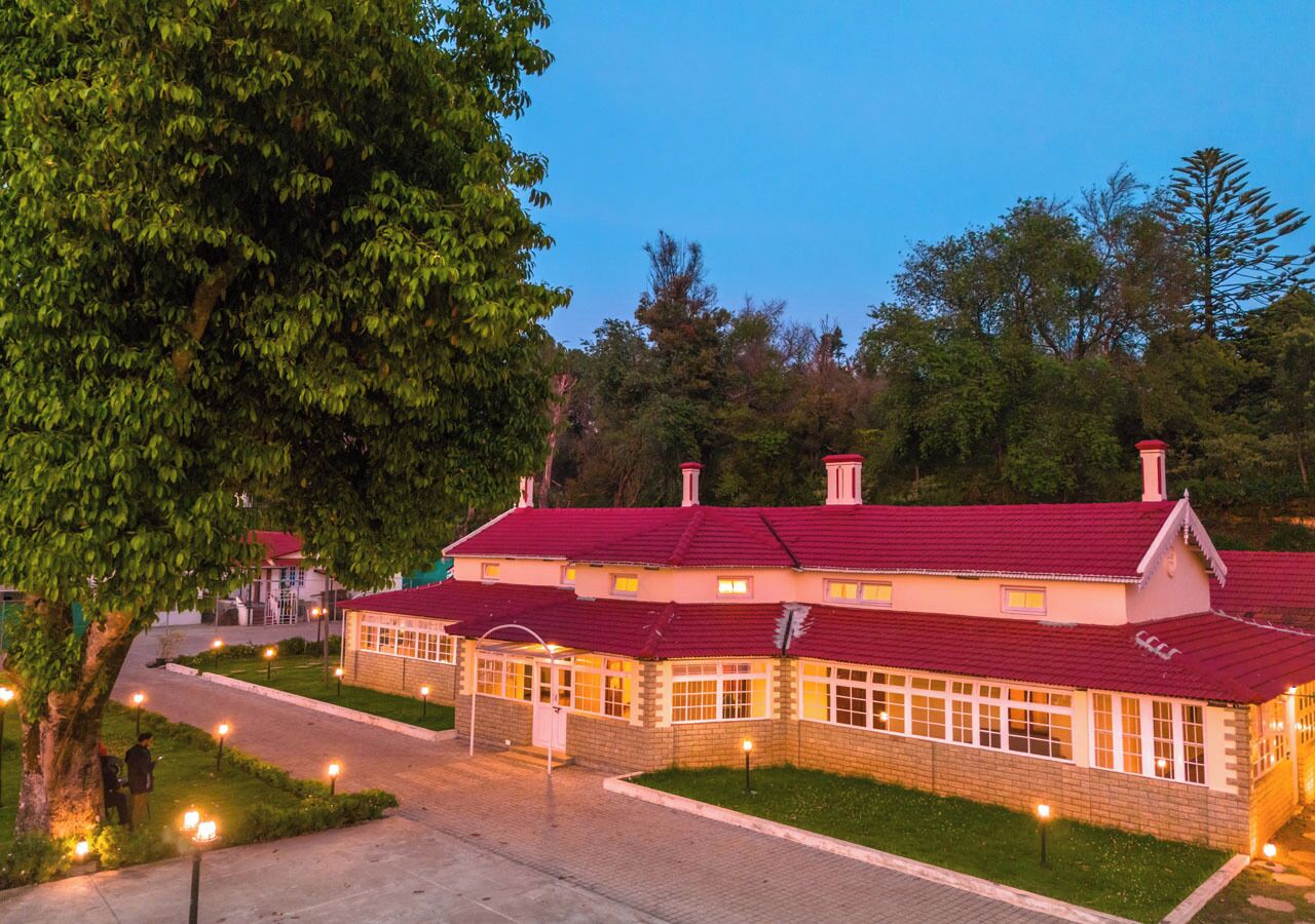 A building with a red roof and multiple windows, surrounded by greenery and a paved walkway.