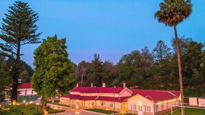 A building with a red roof, surrounded by trees and a well-lit outdoor area with chairs and tables. - Mowbray House Resort Ooty by VOYE HOMES (Ooty)