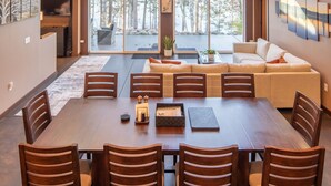 A spacious dining area with a large wooden table and chairs, large windows with a view of trees, and a ceiling fan. - Stone Ridge Retreat Cabin (Danbury)