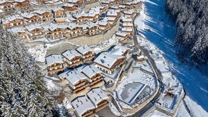 A snow-covered resort with wooden cabins arranged around a central lake, surrounded by forested hills. - Chalet Near Ski Lift With Garden (Neukirchen am Grossvenediger)
