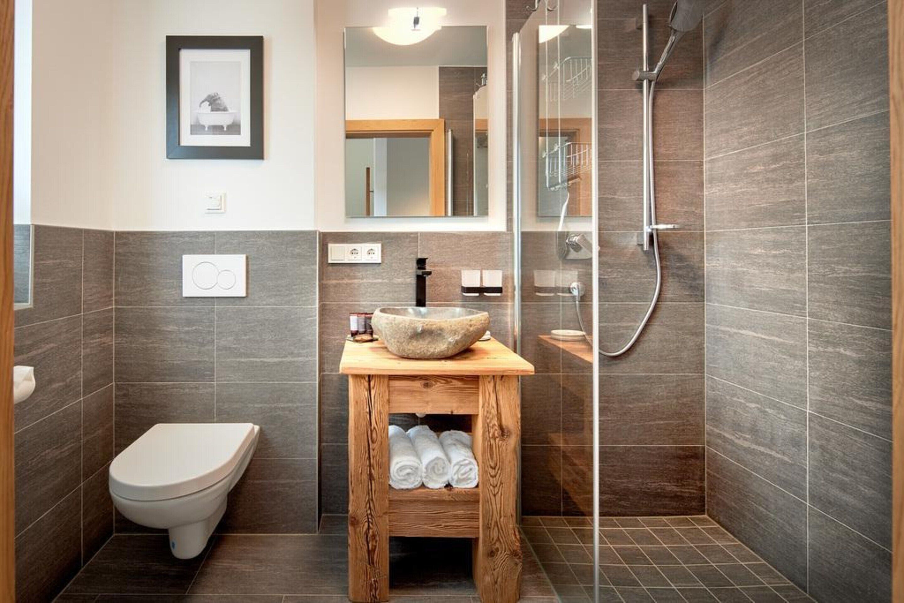 Un baño moderno con un lavabo de piedra, tocador de madera, inodoro y zona de ducha con mampara de vidrio.