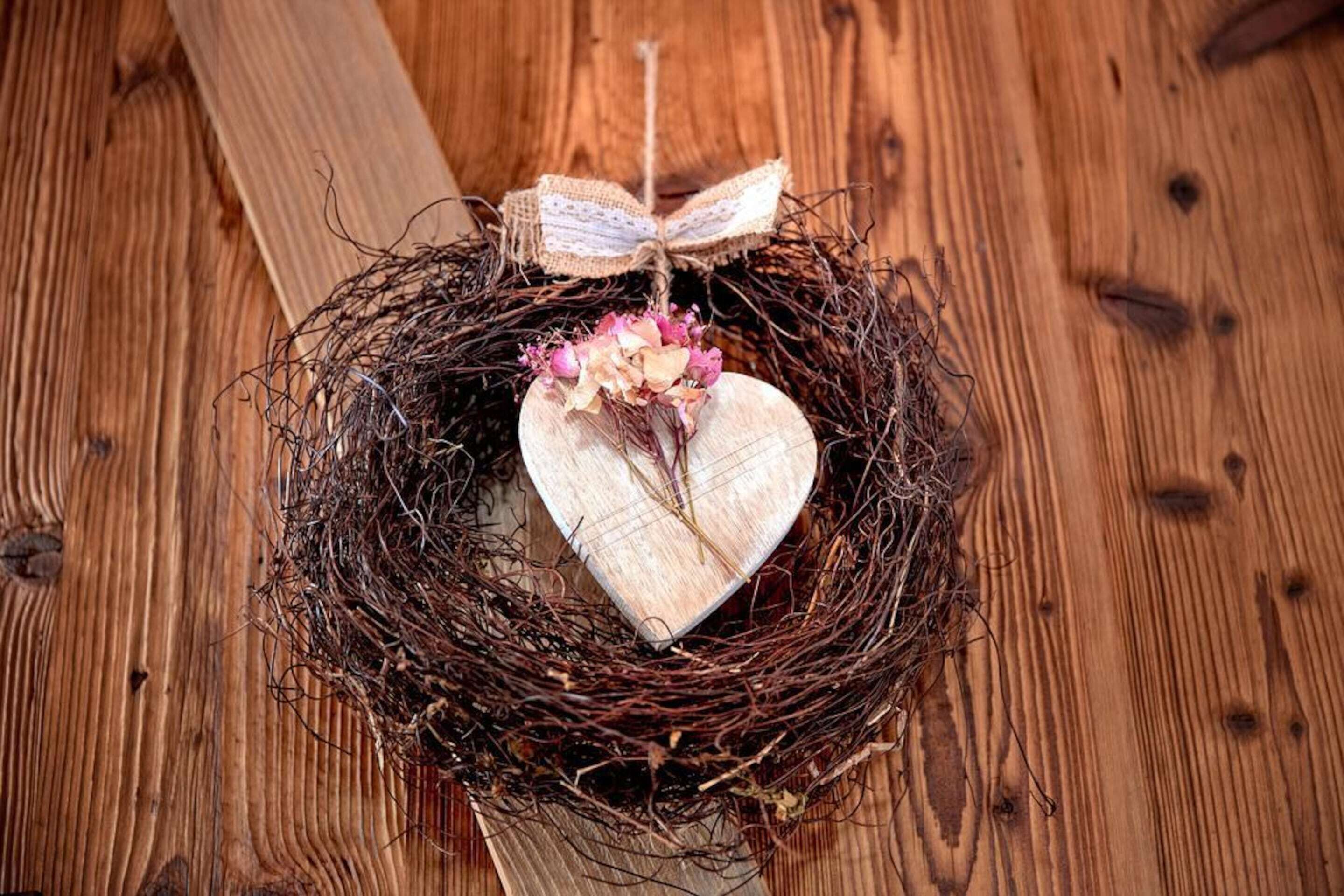 A wooden nest with a heart-shaped object and flowers, tied with a ribbon and a bow.