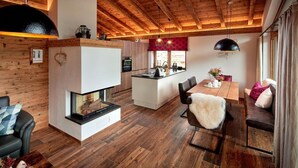 A modern interior with a fireplace, wooden flooring, a dining area, and a kitchen. - Chalet Near Ski Lift With Garden (Neukirchen am Grossvenediger)
