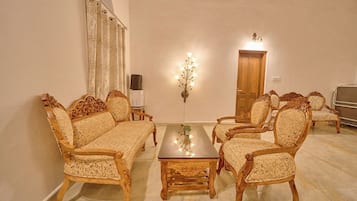A traditional living room with a sofa set, a coffee table, and matching chairs. There is a wooden door and a wall-mounted light fixture.