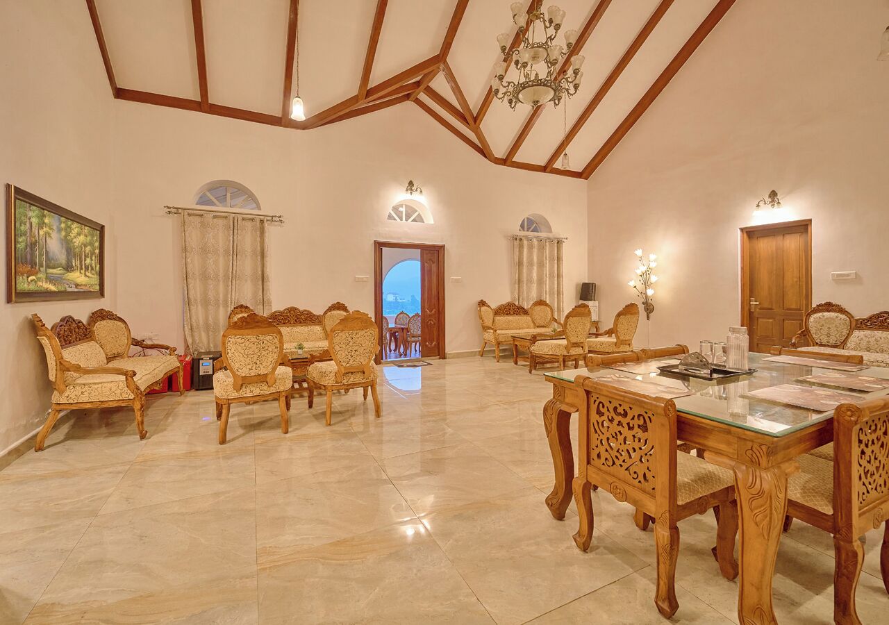A spacious room with a high ceiling, wooden beams, a dining area with a glass table, and several upholstered chairs.