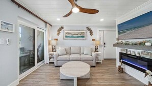 Un salon spacieux avec un grand canapé, une table basse et un ventilateur de plafond. Un tableau orne le mur, et une cheminée avec un manteau de cheminée est également présente.