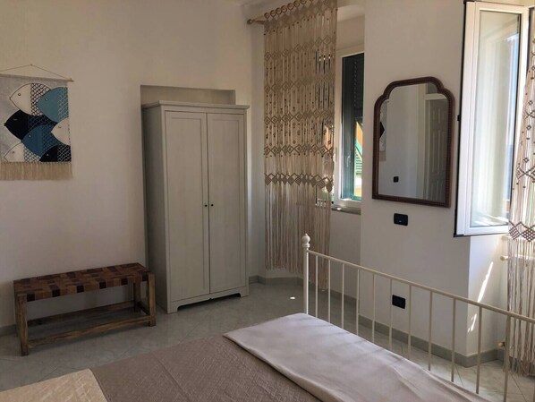 A bedroom with a bed, a wardrobe, a bench, a mirror, and a decorative wall hanging. - Nautilus, Apartment in the Center of Riomaggiore, Near the Sea and the Train Station (Riomaggiore)