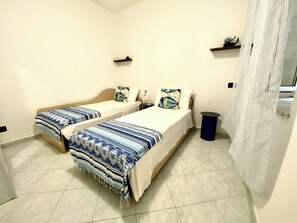 Quarto com duas camas de solteiro, uma pequena lixeira e uma cortina.