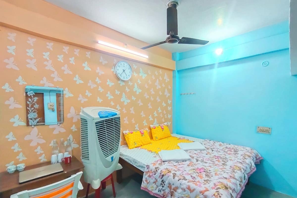 Ein Schlafzimmer mit Bett, Schreibtisch, Stuhl, Wanduhr, Deckenventilator und Schmetterlingsmuster-Tapete.