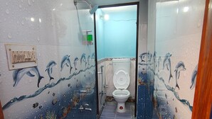 A bathroom with a dolphin mural, a toilet, a shower, and a blue bucket on the floor. - Sneh Homestay (Faizabad)
