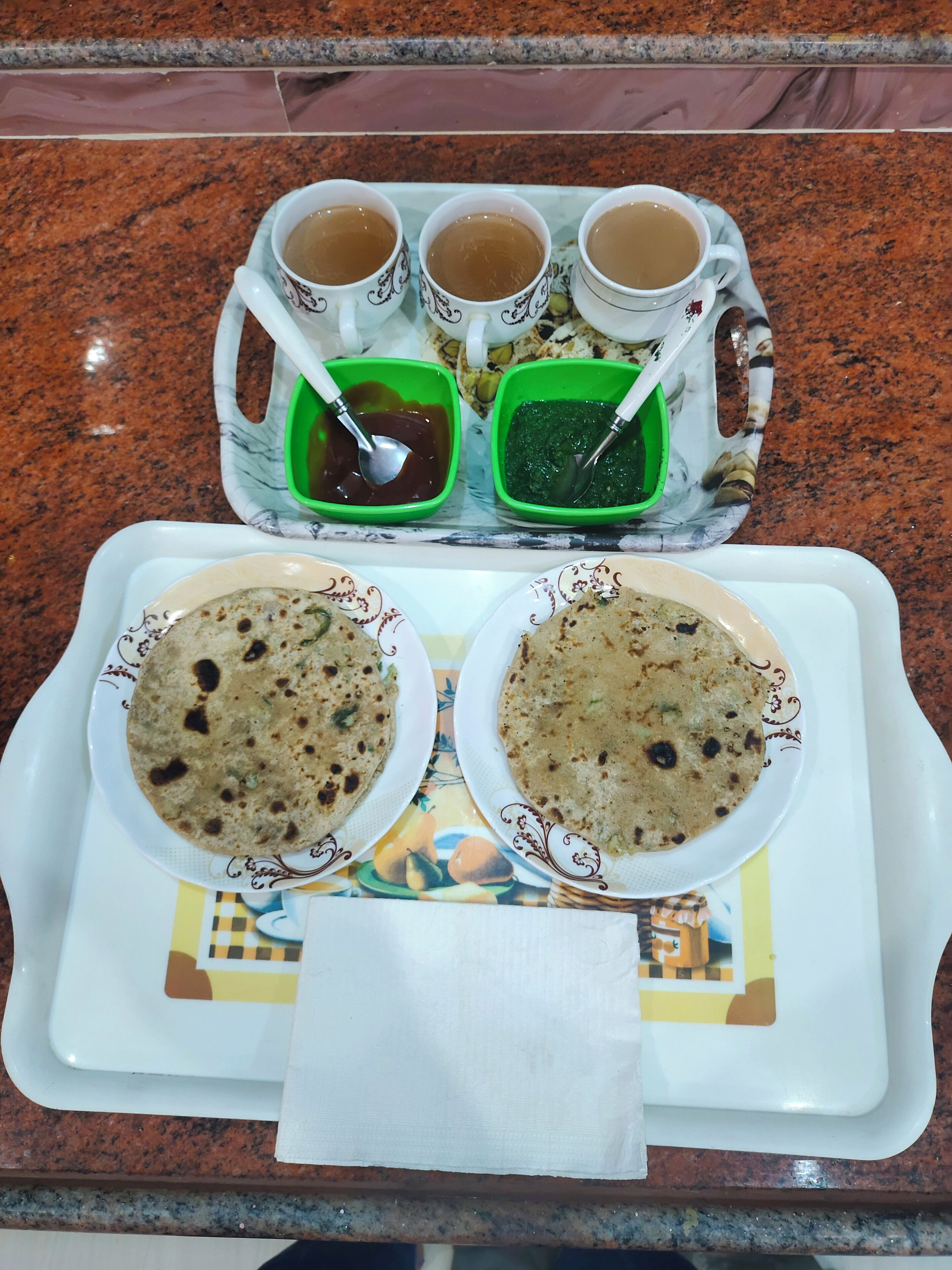 A tray with two bowls of flatbread, three cups of tea, and two green condiment containers.