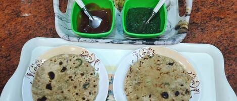 A tray with two bowls of flatbread, three cups of tea, and two green condiment containers.