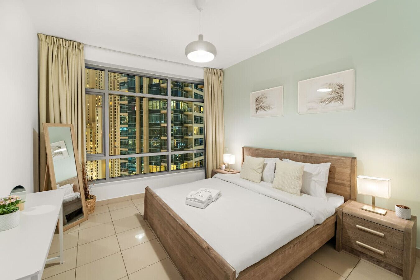 Une chambre d’hôtel avec une grande fenêtre, un lit, une table de chevet, une chaise et un bureau.