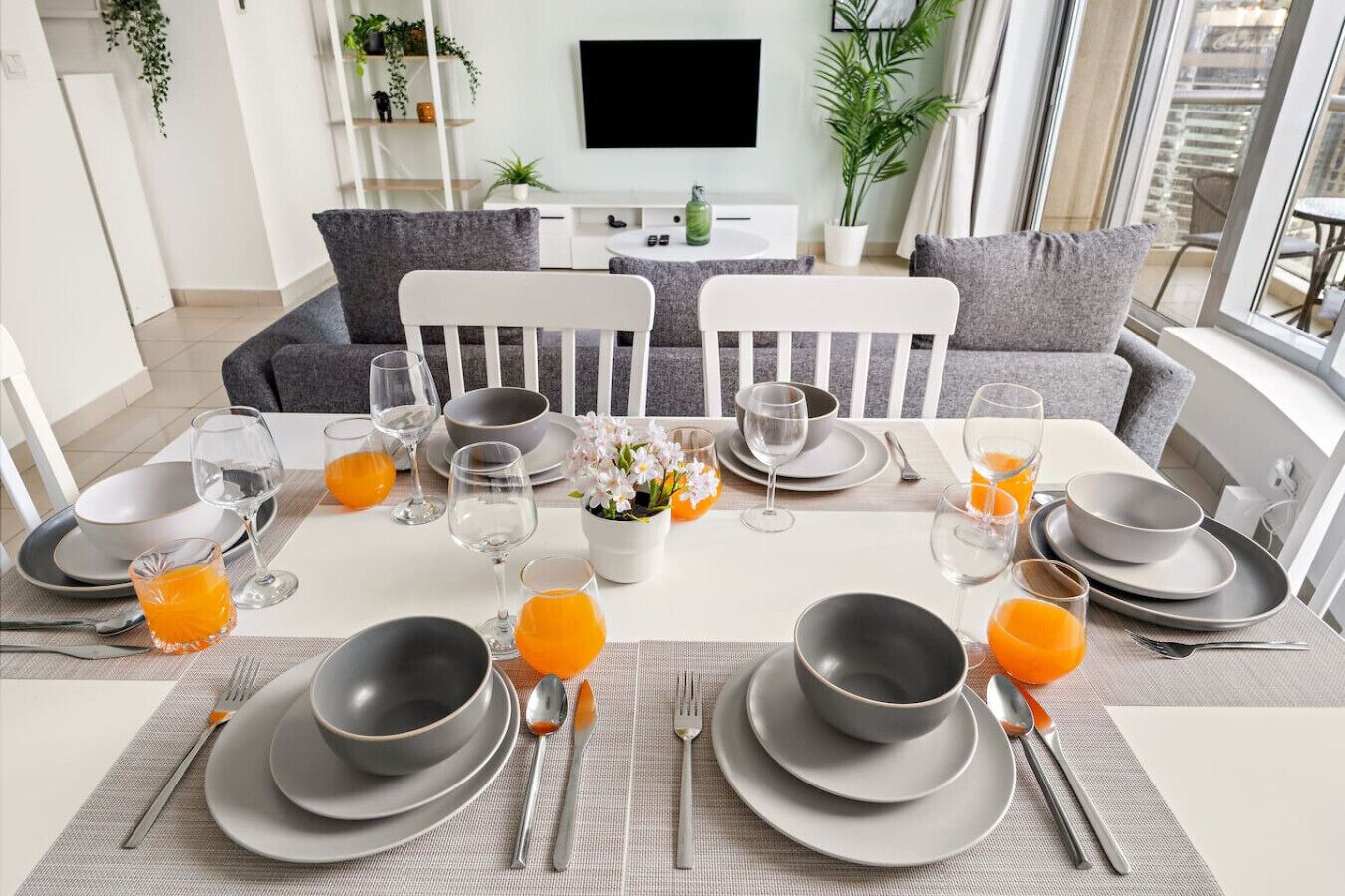 A dining area with a table set for breakfast, including plates, glasses, and orange juice.