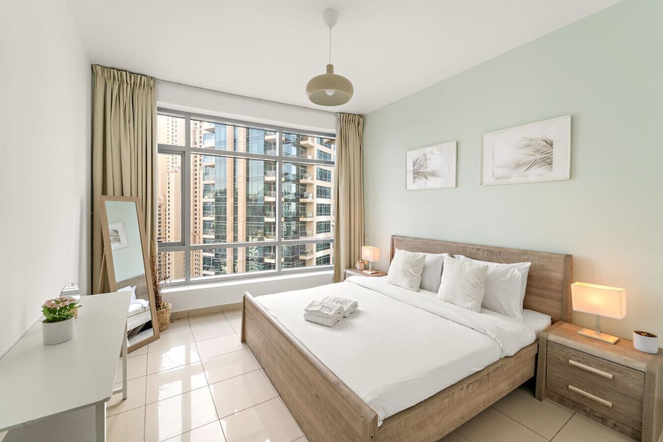 Een moderne hotelkamer met een groot raam, een bed met witte lakens, een houten hoofdbord en twee nachtkastjes met lampen.