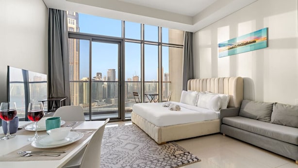 A modern hotel room with a large window offering a city view, a dining area with a table set for two, and a comfortable seating area with a sofa and a bed. - FIRST CLASS | Studio | Chic City Escape (Dubai)