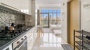A modern kitchen with a gas stove, a dining area with a table and chairs, and a city view through large windows. - FIRST CLASS | Studio | Chic City Escape (Dubai)