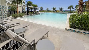 A poolside area with lounge chairs and tables, a clear pool, and a building in the background. - FIRST CLASS | Studio | Chic City Escape (Dubai)