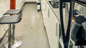 A modern kitchen with white cabinets, a stainless steel refrigerator, a gas stove, and a bar stool.