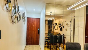 A hallway with a wooden door, a mirror wall, and a dining area with chairs and a table.