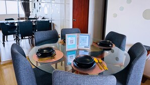 A modern dining area with round glass tables, grey upholstered chairs, and a view of a dining room in the background.