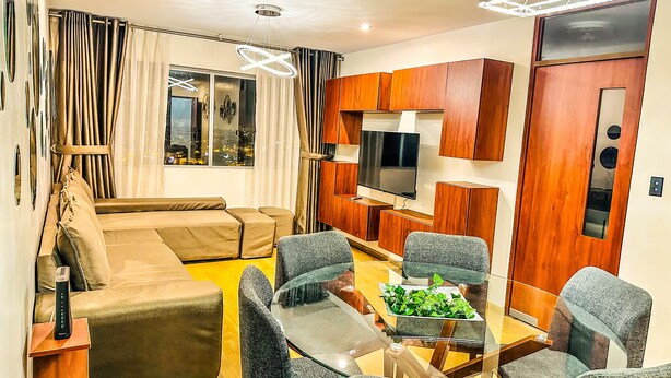 A modern living room with a sofa, a glass coffee table, and a TV mounted on a wooden wall.