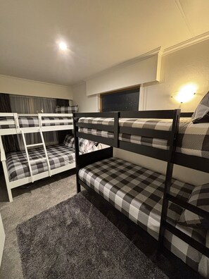 Een slaapkamer met een stapelbed, een geruit matras, een trapje en een wandlamp.
