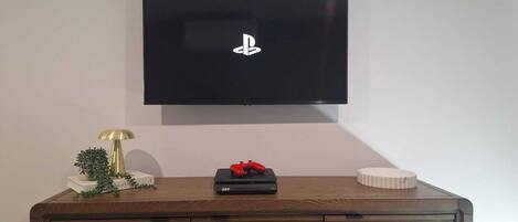 Een flatscreen televisie bevestigd aan een muur boven een houten kastje met een decoratieve lamp, een kleine plant en een rood object.