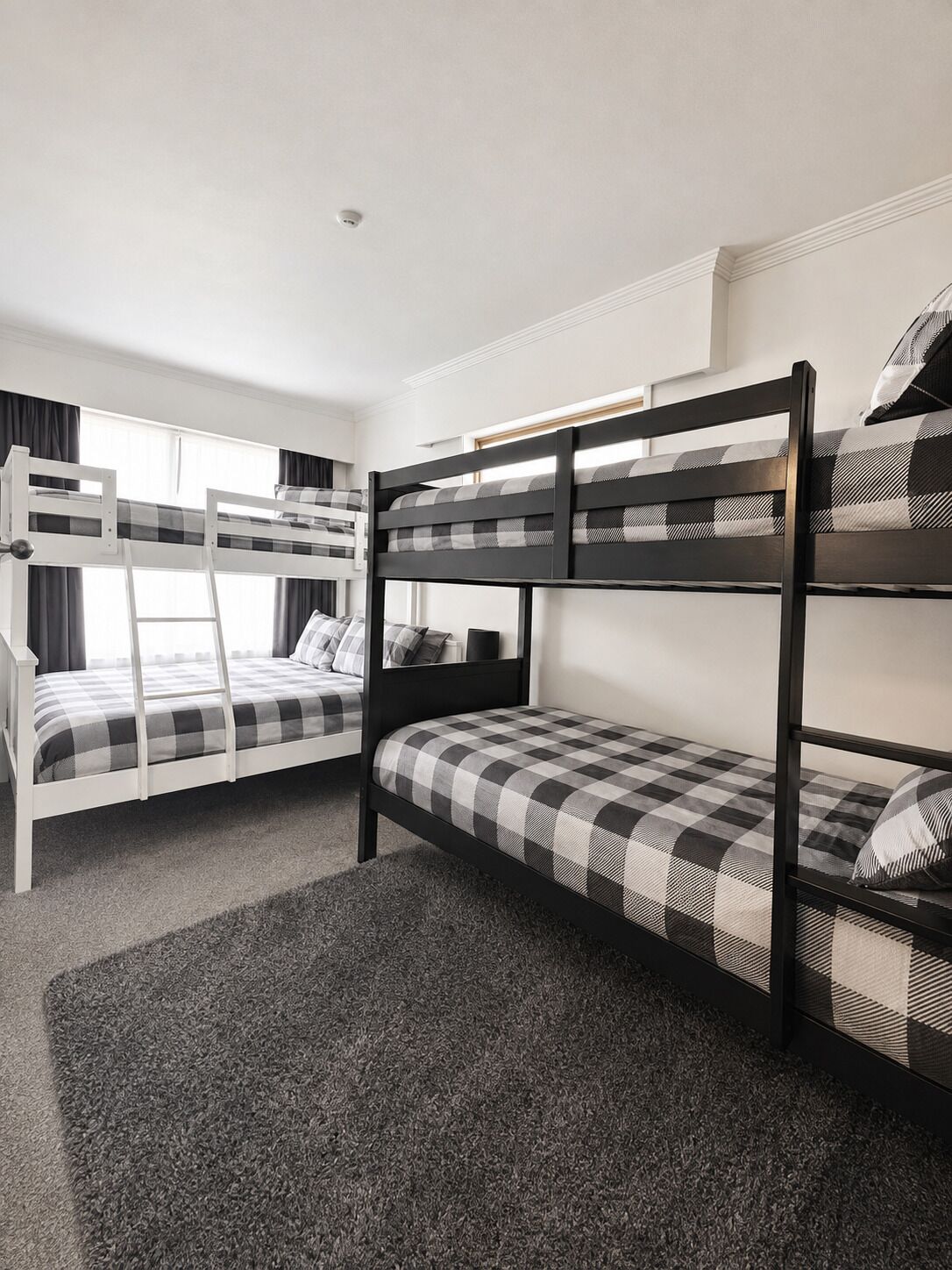 Een kamer met stapelbedden, een raam met gordijnen en een vloerbedekking.