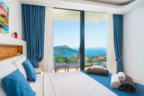 Relax on the balcony with a view of the sea and mountains, featuring a large bed and a small table.