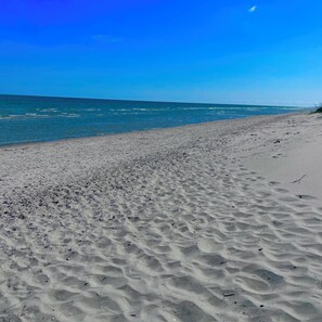 Ein sandiger Strand mit sanften Wellen, blauem Himmel und einer fernen Küstenlinie.
