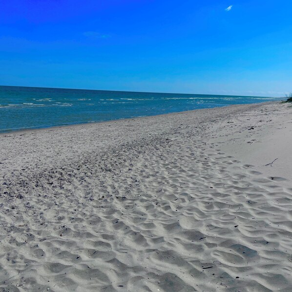 A sandy beach with gentle waves, clear sky, and distant shoreline.