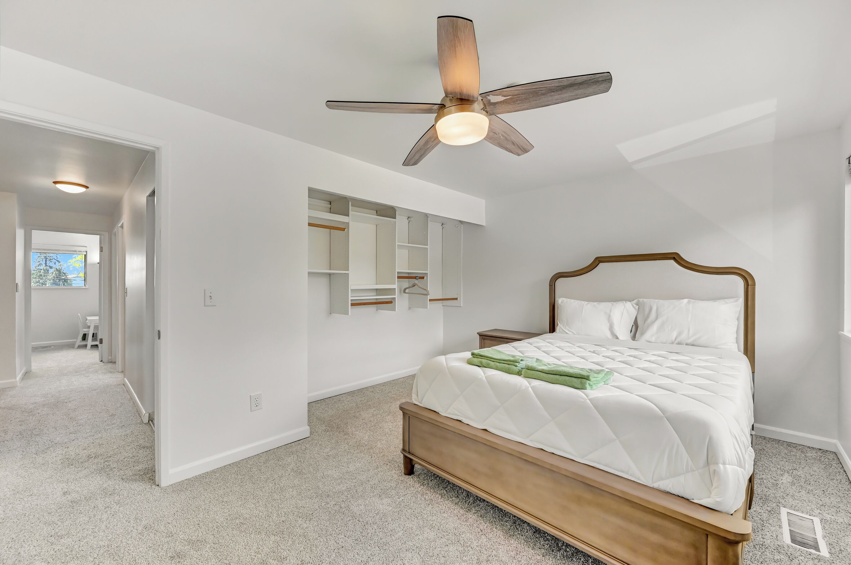 A bedroom with a bed, a ceiling fan, a walk-in closet, and a hallway leading to another room.