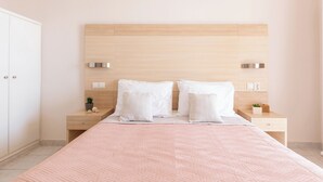 Une chambre à coucher avec une tête de lit en bois, deux oreillers blancs, une couvre-lit rose matelassée, une table de chevet avec une petite plante et un tiroir.