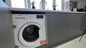 Une cuisine moderne dotée d’un lave-linge encastré, de grandes fenêtres et d’un sol carrelé.
