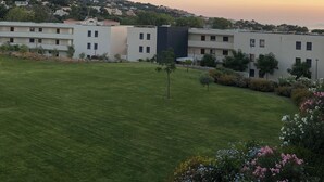 A modern building complex with multiple apartment buildings, a well-maintained lawn, and a view of a hilly landscape in the background.