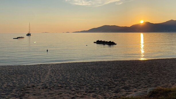 A beach with calm waters, boats, and a sunset.