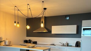A modern kitchen with a central island, bar stools, and a hanging light fixture.