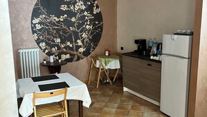 A compact kitchen with a dining area, featuring a large decorative wall piece, a refrigerator, and a small table with chairs. - La Fonte B&B (Baranello)