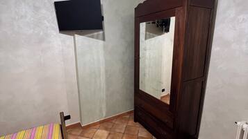 Un dormitorio con cama, armario, televisor y lámpara en el techo.