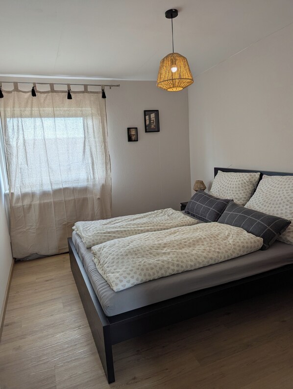 A bedroom with a bed, a hanging light fixture, a window with curtains, and a small framed picture on the wall. - Schweigen-Rechtenbach - Modern "Martina" Vacation Apartment, Ideal for 4 (Schweigen-Rechtenbach)