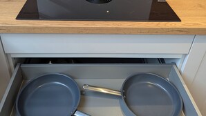 A modern kitchen with a built-in induction cooktop, a wooden countertop, and a drawer with two frying pans. - Schweigen-Rechtenbach - modern vacation apartment "Martina" ideal for four people (Schweigen-Rechtenbach)