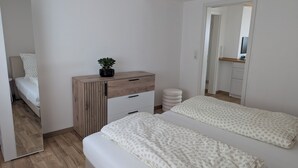 A modern bedroom with a wooden wardrobe, a small round stool, and a potted plant. - Schweigen-Rechtenbach - modern vacation apartment "Martina" ideal for four people (Schweigen-Rechtenbach)