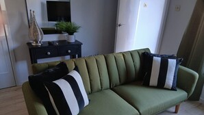 A green sofa with black and white striped pillows, a small potted plant, and a decorative glass vase on a black side table. - Newly refurbished ground floor flat within easy walking distance of town centre. (Inverness)