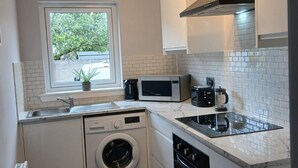 A compact kitchen with a built-in washing machine, a microwave, a coffee maker, and a stove. - Newly refurbished ground floor flat within easy walking distance of town centre. (Inverness)