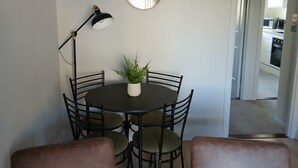 A dining area with a round table, six chairs, a potted plant, a round mirror, and a pendant light. - Newly refurbished ground floor flat within easy walking distance of town centre. (Inverness)